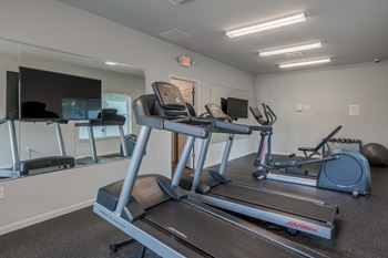 a gym with cardio equipment and a flat screen tv